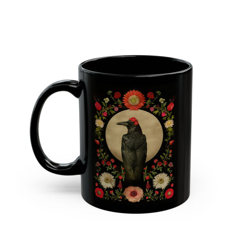 A black ceramic mug featuring a gothic design of a raven against a golden full moon, framed by a floral wreath of coral-colored daisies, white chrysanthemums, and delicate botanical elements. The design includes rich green foliage and small red buds arranged in a symmetrical pattern. The mug has a classic C-shaped handle with a glossy finish.
